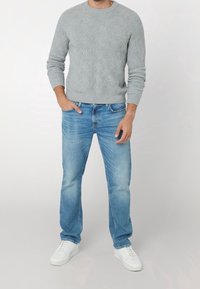 Pull en tricot texturé gris avec un col rond, associé à un jean bleu clair et des baskets blanches. Coupe décontractée avec des détails de couture visibles.