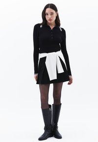 Svart ribbad långärmad polo med vita ränder, ihopparad med en plisserad svart kjol och en vit tröja knuten i midjan; svarta knähöga stövlar.
