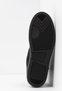 Semelle d'une chaussure noire montrant des motifs de bande de roulement texturés, des designs circulaires et en chevrons, ainsi que le nom de la marque "HUB" avec la taille "37" embossée.