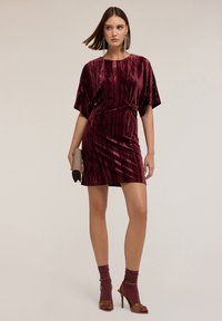 Burgundowa aksamitna sukienka z opiętą talią, krótkimi rękawami i długością do kolan. W zestawie z błyszczącymi skarpetkami i sandałami na obcasie.