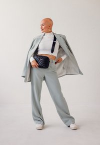 Světle šedé kalhoty na míru zkombinované s bílým crop topem s žebrovaným vzorem. Černá prošívaná kabelka přes rameno visí na popruhu a je zdobena stříbrným řetězem.