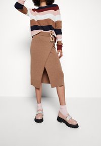 Stickad tröja med horisontella ränder i vinröd, marinblå och rosa. Brun omlotkjol med en sidspänne. Glansiga loafers med en kontrasterande rem.