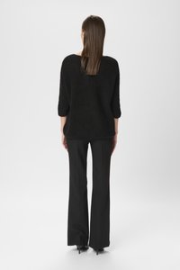 Melns, brīvi adīts džemperis ar trim ceturtajām piedurknēm. Saskaņots ar melniem, pielāgotiem platām biksēm un melnām augstpapēžu kurpēm. Gluda tekstūra.