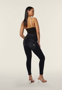 Leggings in denim scuro a vita alta con una finitura liscia, dotati di tasche posteriori e una silhouette aderente. Abbinati a un top nero aderente.