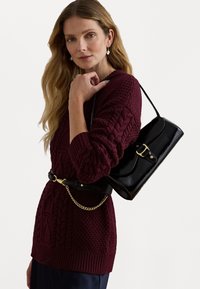 Burgundi árkötéses pulóver hosszú ujjakkal, fekete keresztpántos táskával párosítva, aranyszínű csattal és lánc részletekkel.