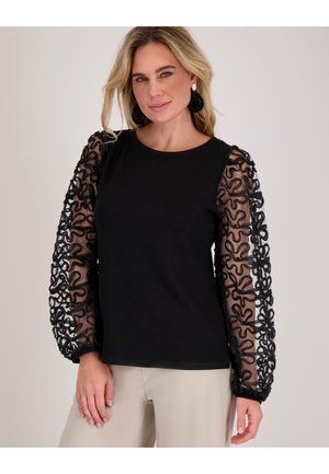 Zwart shirt met lange mouwen van textuur zwart kant met een draaiend patroon. Eenvoudige ronde hals, zachte stof en aansluitende pasvorm.