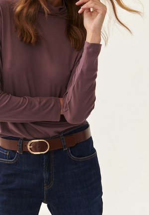 Lange mouw, mauve top gecombineerd met donkerblauwe jeans en een bruine leren riem met een gouden ovale gesp. Gladde textuur, aansluitende stijl.