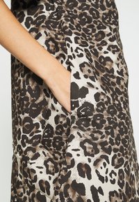 Klänning med leopardmönster i texturerat tyg i nyanser av brunt och beige, med en synlig sidficka på vänster sida.