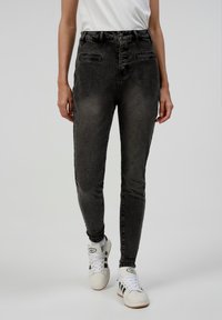 Jeans de mezclilla negros de cintura alta con un acabado desgastado, que cuentan con una tapeta de cinco botones, bolsillos frontales y un diseño ajustado.