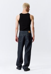 Μαύρο τοπ χωρίς μανίκια με σκούρο μπλε τζιν τζιν. Τα τζιν έχουν ελαφρώς φαρδιά εφαρμογή, πέντε τσέπες και ένα ταμπόν από μαύρο δέρμα στη ζώνη μέσης.