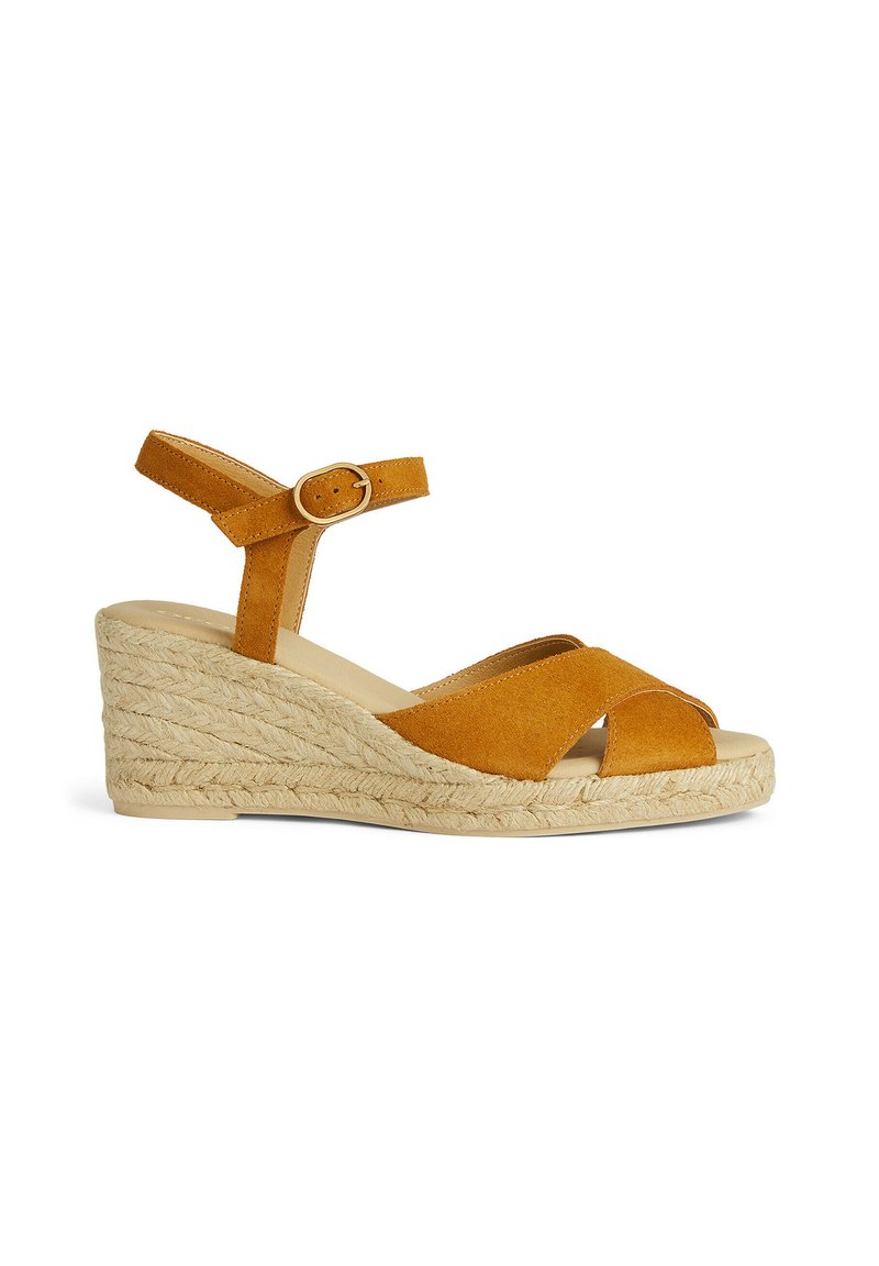 Sandalo con zeppa in suede arancione bruciato, con upper straps incrociate e cinturino alla caviglia. Il tacco impagliato offre texture e altezza.