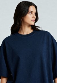 Tamsiai mėlynas per didelis marškinėliai, pagaminti iš minkštos, tekstūruotos medžiagos. Jame yra apvalios iškirptės ir trumpi rankovės su laisvu siluetu.