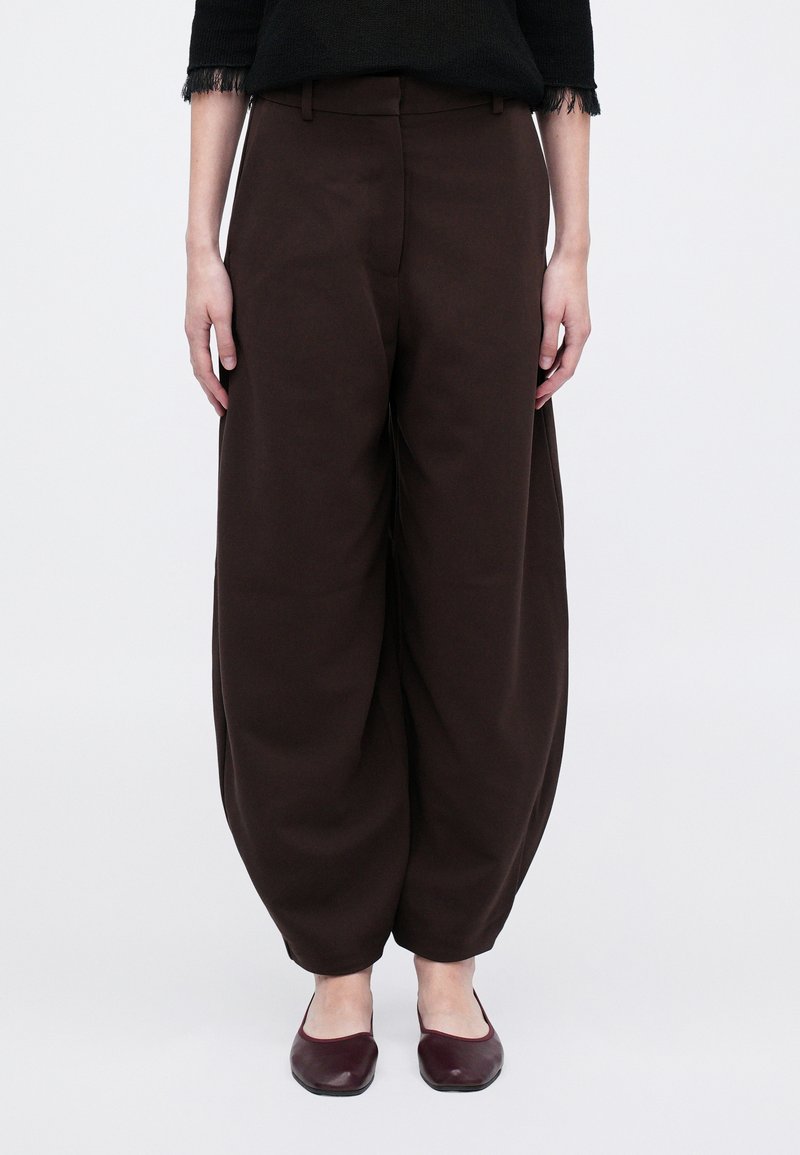 Pantaloni marroni, dalla vestibilità ampia, con una superficie liscia e design a gamba dritta. Stilizzati con vita alta e nessuna ferramenta visibile.