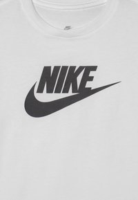 Camiseta de algodón blanca con un gran logo negro de Nike y un diseño de swoosh. El escote es acanalado para mayor textura.