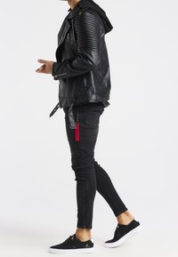Giubbotto in pelle nera da moto con dettagli a coste sulle spalle, abbinato a jeans skinny neri con ginocchio strappato e sneakers nere.