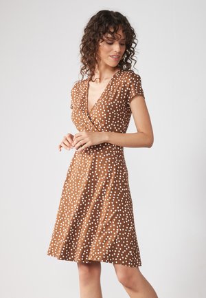 Robe à pois marron avec un décolleté en V et des manches courtes, présentant un corsage ajusté et une jupe évasée. Tissu doux et texturé.