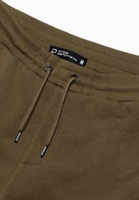 Olivgrüne Sweatpants mit einem Kordelzugbund, ausgestattet mit schwarzen Ösen und einem Etikett, das "Ombre Performance" in weißem Text zeigt.