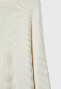 Pull tricoté couleur crème avec une texture côtelée sur le corps, les manches et l'encolure, présenté sur un fond uni clair.