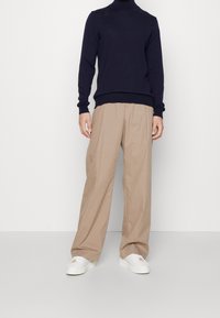 Marinblå turtleneck-tröja, beige vida byxor och vita sneakers. Outfiten har en tät passform i midjan och en avslappnad silhuett.