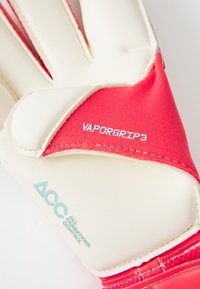 Kapus kesztyű fehér latex tenyérrel, piros textil hátrészsel és kék logóval. Erősített varrással és 'VAPORGRIP3' címkével rendelkezik.