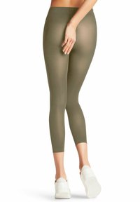 Leggings verde oliva a vita alta con una texture liscia e elastica, di lunghezza cropped e design aderente. Indossati con sneakers bianche e chunky.