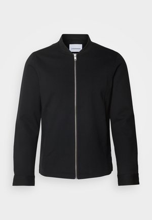 Chaqueta negra con cremallera y cuello alzado, mangas largas, tejido suave y dobladillos con puños. Diseño minimalista con herrajes funcionales.