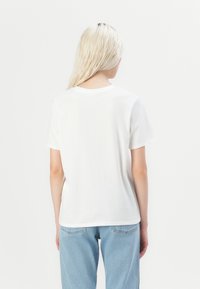 T-shirt en coton blanc à manches courtes, col rond et coupe décontractée, associé à un jean en denim bleu clair.
