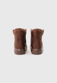 Botas de tobillo acolchadas marrones con un acabado suave, paneles laterales elásticos y suelas de goma. Presenta un parche con el logo en el lado exterior.