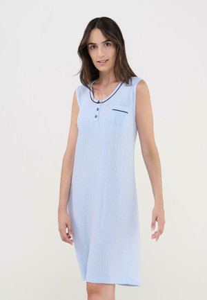 Mujer con vestido sin mangas azul claro de canalé, con escote abotonado y pequeño bolsillo en el pecho con ribete oscuro, de pie frente a un fondo liso.