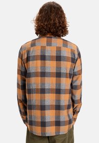 Geruite shirt in oranje, grijs en zwart. Gemaakt van zachte stof met lange mouwen, knopen manchet en een ronde zoom. Opvallend ruitpatroon.