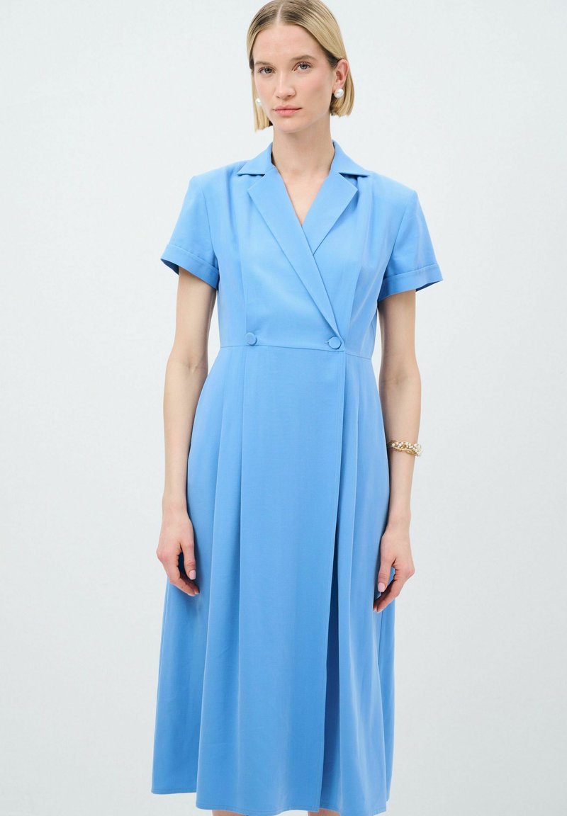 Robe bleu clair à manches courtes, devant double boutonnage, jupe plissée et texture douce. Présente un col et un design élégant.