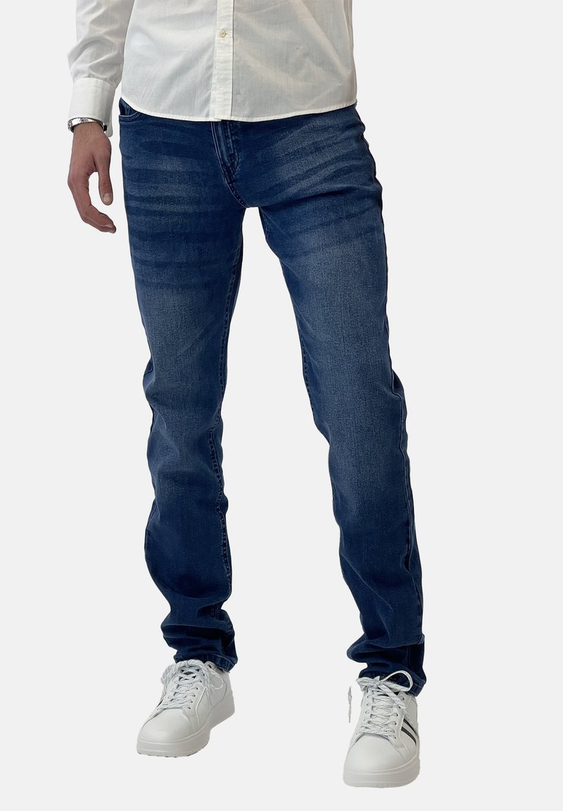 Jeans azul oscuro de corte slim y un ligero desgastado, combinados con zapatillas blancas. La textura es denim suave con costuras cosidas.