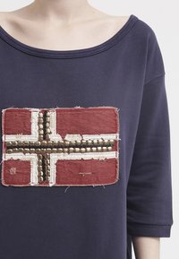 Felpa blu navy con toppa ricamata raffigurante una bandiera rossa, arricchita da paillettes beige e metalliche e bordi sfrangiati.