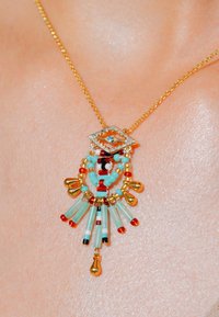 Collier en or avec un pendentif en forme de diamant présentant un motif d'œil. Perles colorées en rouge, noir et turquoise, avec des accents pendants.