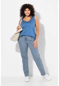 Top blu, senza maniche, abbinato a jeans azzurri chiari. I jeans sono a taglio dritto con tasche. Sneakers bianche e una borsa beige completano l'outfit.