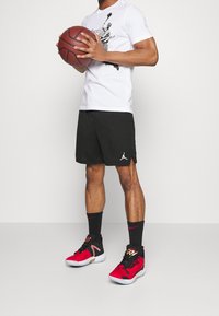 White t-shirt with black graphic, black athletic shorts, and red and black sneakers. Ball held in hands. Focus on sportswear elements.
