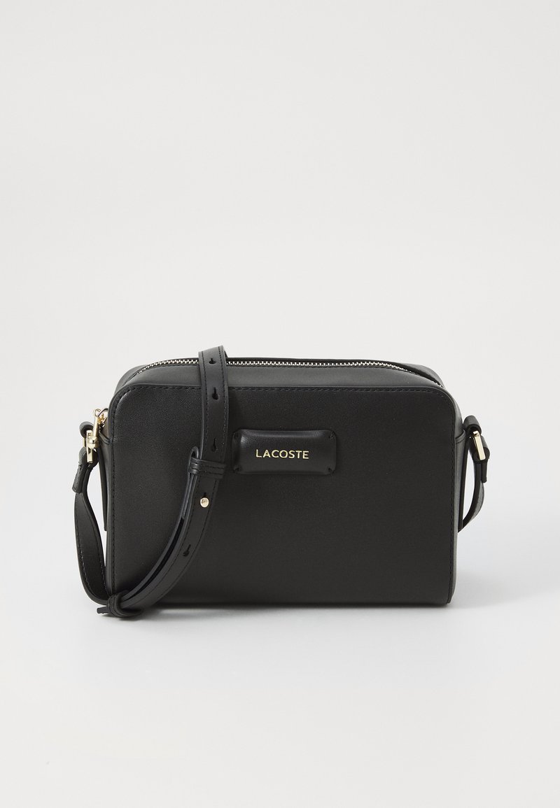 Borsa a tracolla nera in pelle con chiusura a zip, accessoriati in oro e patch logo anteriore. Presenta una tracolla regolabile per un uso versatile.