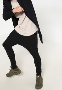 Svarta joggerbyxor med en avslappnad passform och ribbad textur, i kombination med en beige topp och gröna sportskor, som visar upp en lager-look.