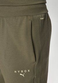 Olivgrüne Jogginghosen aus weichem Material. Mit seitlichen Taschen, einem elastischen Bund und dem bedruckten "HYROX"- und Wolkenlogo in heller Farbe.