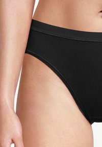 Unterkörper und Oberschenkel einer Frau, die einfache schwarze Baumwollunterwäsche mit elastischem Bund trägt.