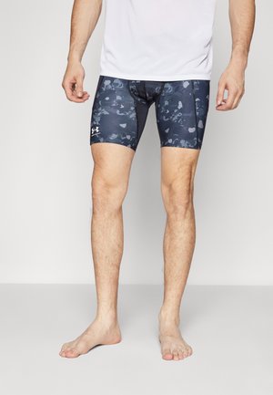Tætsiddende, mørkeblå badeshorts med camouflagemønster, lavet af strækbart materiale. Har en logo på venstre side og en glat overflade.