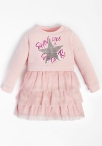 Růžové šaty s dlouhými rukávy, zdobené stříbrnou hvězdou a třpytivým textem. Sukně z tylu s vrstvenými volány přidává texturu. Měkký textilní materiál.