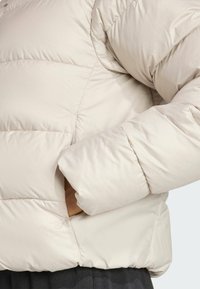A close-up of a cream-colored puffer jacket with a hand in the side pocket, showcasing the fabric's texture and stitching details.