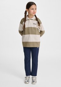 Randig långärmad polo i grön och beige, med krage och logotyp på vänster bröst. Matchad med marinblå byxor och silverfärgade sneakers.