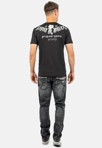 Zwarte katoen T-shirt met witte grafische tekst op de achterkant. Draagt met vervaagde grijze denim jeans met gedetailleerde stiksels en zakken.