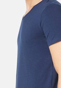 Mørkeblå kortærmet t-shirt med v-hals design, lavet af glat stof. Har en tætsiddende form og blød tekstur.
