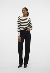 Gestreepte langemouwen shirt in crème en zwart, gecombineerd met hoge zwarte jeans. Het model draagt puntige zwarte schoenen en grote hoepel oorbellen.