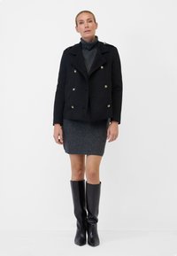 Black double-breasted peacoat with golden buttons, worn over a fitted gray rib-knit dress, paired with knee-high black boots.
