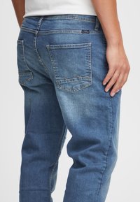 Tamsiai mėlynos spalvos džinsai iš džinso audinio, turintys laisvą kirpimą, penkias kišenes ir siuvinėjimus ant galinių kišenių su subtiliu išblukimo efektu.