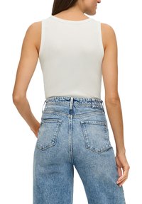 Top bianco senza maniche con scollatura rotonda, abbinato a jeans in denim azzurro chiaro a vita alta con tasche posteriori e una vestibilità rilassata.